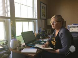 This April 3, 2020 photo shows realtor Michelle Bushée posing at her desk while working from her home in Pittsburgh, Pa. Bushee has always been an avid planner. Her weeks used to be very busy but now the entire month of April is empty. (Nick Bushée via AP)