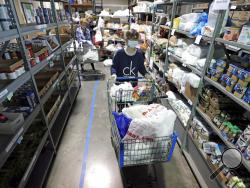 In this April 9, 2020, photo, worker Laura Burbank pushes a cart filled with food for a family through the pantry at GraceWorks Ministries food pantry in Franklin, Tenn. The coronavirus pandemic has provoked a spike in demand for food pantries in the U.S. (AP Photo/Mark Humphrey)