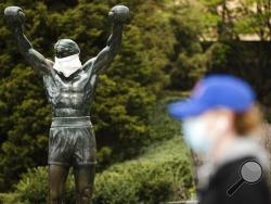 FILE - In this April 14, 2020, file photo, a person wearing a protective face mask as a precaution against the coronavirus walks past the Rocky statue outfitted with mock surgical face mask at the Philadelphia Art Museum in Philadelphia. (AP Photo/Matt Rourke, File)