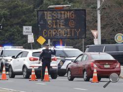 FILE - In this March 20, 2020, file photo, a police officer waves traffic past the entrance to a drive-thru coronavirus testing center after it reached capacity, in Paramus, N.J. Feeling sick and stressed, people in the states hardest hit by the coronavirus have continued to stream into drive-thru testing sites, hoping to get guidance about whether to seek treatment, or reassurance that they aren’t infected. (AP Photo/Seth Wenig, File)