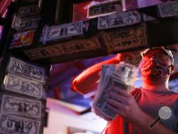 In this Thursday, April 16, 2020 photo, Tyler Stalvey removes one dollar bills from the wall at the Boar's Head Lounge in downtown Athens, Ga. The dollars are being removed and will go to staff after the bar closed to prevent the spread of the coronavirus. The tradition of placing marked bills on the wall started back in 1997 when the bar opened. (Joshua L. Jones,/Athens Banner-Herald via AP)