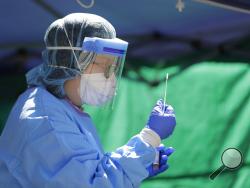 Tina Nguyen, a nurse at at the International Community Health Services clinic in Seattle's International District, examines a nose swab while conducting walk- and drive-up testing for COVID-19, Friday, May 15, 2020. As testing supplies for coronavirus have become more abundant, the clinic has been able to offer testing to anyone in the community by appointment if they are experiencing symptoms. (AP Photo/Ted S. Warren)