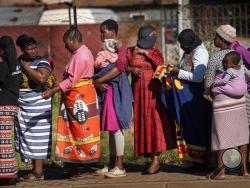 FILE- In this file photo taken Thursday, April 30, 2020, Women carrying their children lineup to receive vegetables from the Jan Hofmeyer community services in the Vrededorp neighborhood of Johannesburg. South Africa is struggling to balance its fight against the coronavirus with its dire need to resume economic activity. The country with the Africa’s most developed economy also has its highest number of infections — more than 19,000. (AP Photo/Jerome Delay, file)