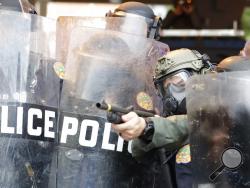 A policeman shoots rubber bullets at protesters throwing rocks and water bottles during a demonstration next to the city of Miami Police Department, Saturday, May 30, 2020, downtown in Miami. Protests were held throughout the country over the death of George Floyd, a black man who died after being restrained by Minneapolis police officers on May 25. (AP Photo/Wilfredo Lee)