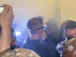 In this image made from video released by Jonathan Maus, Portland Mayor Ted Wheeler, center in black with goggles looking away, stands at a fence guarding a federal courthouse as tear gas drifts by early July 23, 2020, in Portland Oregon, during another night of protest against the presence of federal agents sent by President Donald Trump to quell unrest in the city. (Jonathan Maus/BikePortland via AP)