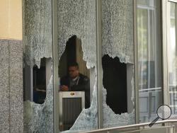 A man sits behind a broken glass from a window at the Ronald V. Dellums Federal Building in Oakland, Calif., Sunday, July 26, 2020. A protest through the streets of downtown Oakland, California, in support of racial justice and police reform turned violent when "agitators" among the demonstrators set fire to a courthouse, vandalized a police station and shot fireworks at officers, authorities said. (AP Photo/Jeff Chiu)