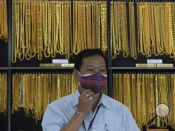 FILE - In this April 16, 2020, file photo, a Thai shopkeeper adjusts his face mask at a gold shop in Bangkok, Thailand. The price of gold surged more than $30 on Monday, July 27, 2020 to over $1,926 per ounce as investors step up buying of the precious metal often sought in times of uncertainty. Gold was trading at $1,926.20 by early afternoon in Asia, up 1.5%, after surging over the weekend. (AP Photo/Sakchai Lalit, File)