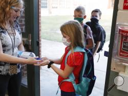 FILE - In this Aug. 5, 2020, file photo, wearing masks to prevent the spread of COVID19, elementary school students use hand sanitizer before entering school for classes in Godley, Texas. As schools reopen around the country, their ability to quickly identify and contain coronavirus outbreaks before they get out of hand is about to be put to the test. (AP Photo/LM Otero, File)