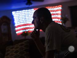 Scott Rice sits in his living room watching a Fox News Channel interview with President Donald Trump in Appleton, Wis., Aug. 20, 2020. Nothing can shake Rice's faith that Trump will save the U.S. economy, not seeing businesses close or friends furloughed, not even his own hellish bout with the coronavirus. But in Appleton, a city of 75,000 people along the Fox River, the health of economy isn't judged on jobs numbers, personal bank accounts or union contracts. Instead, it's viewed through partisan lenses, f