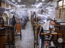FILE - In this Monday, Sept 21, 2020 file photo, ultra-Orthodox Jews wear face masks during a morning prayer in a synagogue separated by plastic partitions, in Bnei Brak, Israel. For Israel's ultra-Orthodox Jews, coronavirus restrictions have raised numerous questions about how to maintain their religious lifestyle during the outbreak. A religious publisher in Jerusalem released a book in July with over 600 pages of guidance from 46 different rabbis. (AP Photo/Oded Balilty, File)