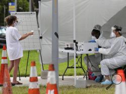 FILE - In this Friday, July 17, 2020 file photo, health care workers take information from people in line at a walk-up COVID-19 testing site during the coronavirus pandemic in Miami Beach, Fla. After months of struggling to ramp up coronavirus testing, the U.S. is now capable of testing some 3 million people daily thanks to a growing supply of rapid tests. But the testing boom comes with a new challenge: keeping track of the results. (AP Photo/Lynne Sladky)