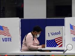 FILE - In this Nov. 3, 2020, file photo, a woman votes at the MLB Urban Youth Academy in Kansas City, Mo. U.S. voters went to the polls starkly divided on how they see President Donald Trump’s response to the coronavirus pandemic, with a surprising twist. In places where the virus is most rampant now, Trump enjoyed enormous support. (AP Photo/Charlie Riedel, File)