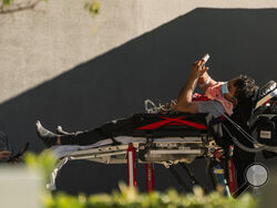 An unidentified patient uses his mobile phone while receiving oxygen on a stretcher, as Los Angeles Fire Department Paramedics monitor him outside the Emergency entrance, waiting for his room at the CHA Hollywood Presbyterian Medical Center in Los Angeles Friday, Dec. 18, 2020. Increasingly desperate California hospitals are being "crushed" by soaring coronavirus infections, with one Los Angeles emergency doctor predicting that rationing of care is imminent. (AP Photo/Damian Dovarganes)