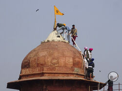 Sikhs hoist a Nishan Sahib, a Sikh religious flag, on a minaret of the historic Red Fort monument in New Delhi, India, Tuesday, Jan. 26, 2021. Tens of thousands of protesting farmers drove long lines of tractors into India's capital on Tuesday, breaking through police barricades, defying tear gas and storming the historic Red Fort as the nation celebrated Republic Day. (AP Photo/Dinesh Joshi)