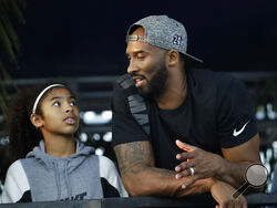 FILE - In this July 26, 2018, file photo, former Los Angeles Laker Kobe Bryant and his daughter Gianna watch the U.S. national championships swimming meet in Irvine, Calif. Federal safety officials are expected to vote Tuesday, Feb. 9, 2021, on what likely caused the helicopter carrying Kobe Bryant, his 13-year-old daughter and seven others to crash into a Southern California hillside last year, killing all aboard. (AP Photo/Chris Carlson, file)