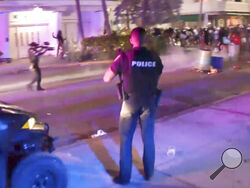 In this image taken from video, SWAT officers in bulletproof vests disperse pepper spray balls on Saturday evening, March 20, 2021, to break up rowdy, spring break crowds that descended on Miami's South Beach by the thousands, trashing restaurants and flooding the streets without masks or social distancing despite COVID-19 restrictions. After days of partying and confrontations between police and large crowds, Miami Beach officials have ordered an emergency curfew. (WPLG via AP)