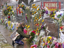A mourner leaves a bouquet of flowers along a fence put up around the parking lot where a mass shooting took place in a King Soopers grocery store Tuesday, March 23, 2021, in Boulder, Colo. (AP Photo/David Zalubowski)