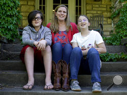 Heather Ousley sits with her older children Elliannah, 15, right, and Samuel, 13, in front of their home in Merriam, Kan, Tuesday, May 4, 2021. Ousley was thrilled when she heard the FDA was expected to authorize Pfizer's COVID-19 vaccine for youngsters ages 12 to 15 and was hoping to get her kids vaccinated as soon as she can. (AP Photo/Charlie Riedel)