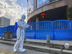 FILE - In this Feb. 6, 2021, file a worker in protectively overalls and carrying disinfecting equipment walks outside the Wuhan Central Hospital where Li Wenliang, the whistleblower doctor who sounded the alarm and was reprimanded by local police for it in the early days of Wuhan's pandemic, worked in Wuhan in central China. U.S. intelligence agencies remain divided on the origins of the coronavirus but believe China's leaders did not know about the virus before the start of the global pandemic, according t