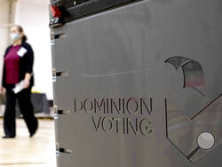 FILE - In this Jan. 4, 2021, file photo a worker passes a Dominion Voting ballot scanner while setting up a polling location at an elementary school in Gwinnett County, Ga., outside of Atlanta. Republican efforts to question the results of the 2020 election have led to two significant breaches of voting software that have alarmed election security experts who say they have increased the risk to elections in jurisdictions that use the equipment. (AP Photo/Ben Gray, File)