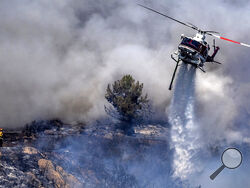 A firefighter is dwarfed by an aerial drop at the the Chaparral Fire in Murrieta which still blazes, Sunday, August 29, 2021. Several homes appear to be evacuated in the area. (Cindy Yamanaka/The Orange County Register via AP)
