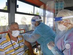 FILE - In this Sept. 4, 2021, file photo, a man receives the Johnson & Johnson vaccine in a bus that serves as a mobile COVID-19 vaccination unit in Bucharest, Romania. In both the U.S. and the EU, officials are struggling with the same question: how to boost vaccination rates to the max and end a pandemic that has repeatedly thwarted efforts to control it. In the European Union, officials in many places are requiring people to show proof of vaccination, a negative test or recent recovery from COVID-19 to p