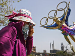 FILE - In this May 2, 2021, file photo, a woman adjusts her face mask as she walks by a statue featuring the Beijing Winter Olympics figure skating on display at the Shougang Park in Beijing. China's "zero tolerance" strategy of trying to isolate every case and stop transmission of the coronavirus has kept kept the country where the virus first was detected in late 2019 largely free of the disease. (AP Photo/Andy Wong, File)