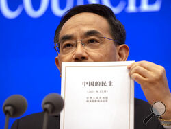 Xu Lin, vice minister of the Publicity Department of the Central Committee of China's Communist Party holds a copy of a government-produced report titled "Democracy that Works" during a press conference at the State Council Information Office in Beijing, Saturday, Dec. 4, 2021. China's Communist Party took American democracy to task on Saturday, sharply criticizing a global democracy summit being hosted by President Joe Biden next week and extolling the virtues of its governing system. (AP Photo/Mark Schief