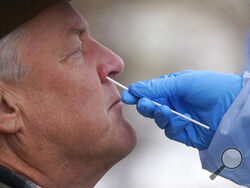 A member of the Salt Lake County Health Department COVID-19 testing staff performs a test on Gary Mackelprang outside the Salt Lake County Health Department Tuesday, Jan. 4, 2022, in Salt Lake City. (AP Photo/Rick Bowmer)