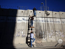 FILE - Palestinians use a ladder to climb over the separation barrier with Israel on their way to pray at the al-Aqsa Mosque in Jerusalem during the Muslim holy month of Ramadan, in Al-Ram, north of Jerusalem, July 11, 2014. Israel on Monday, Jan. 31, 2022, called on Amnesty International not to publish an upcoming report accusing it of apartheid, saying the conclusions of the London-based international human rights group are “false, biased and antisemitic.” (AP Photo/Majdi Mohammed, File)