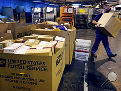 FILE - A worker carries a large parcel at the United States Postal Service sorting and processing facility Nov. 18, 2021, in Boston. Congress would lift onerous budget requirements that have helped push the Postal Service deeply into debt and would require it to continue delivering mail six days per week under bipartisan legislation that approached House approval Tuesday, Feb. 8, 2022. (AP Photo/Charles Krupa, File)