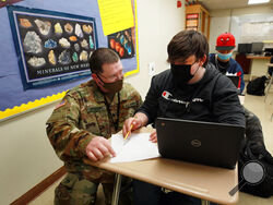New Mexico Army National Guard specialist Michael Stockwell kneels while helping Alamogordo High School freshman Aiden Cruz with a geology assignment, at Alamogordo High School,Tuesday, Feb. 8, 2022, in Alamogordo, N.M. Dozens of National Guard Army and Air Force troops in New Mexico have been stepping in for an emergency unlike others they have responded to before: the shortage of teachers and school staff members that have tested the ability of schools nationwide to continue operating during the coronavir