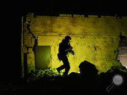 A Ukrainian special police officer walks next to a destroyed building as he patrols during night curfew in Kharkiv, Ukraine, Sunday, March 27, 2022. (AP Photo/Felipe Dana)