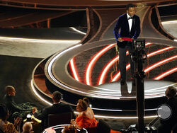 Presenter Chris Rock, right, speaks onstage as Jada Pinkett Smith and Will Smith, bottom left, look on after Smith went onstage and slapped Rock at the Oscars, Sunday, March 27, 2022, at the Dolby Theatre in Los Angeles. (AP Photo/Chris Pizzello)