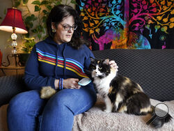 Tara Kramer sits in her apartment with her cat Busy, Friday, April 8, 2022, in Des Moines, Iowa. Month by month, more of the roughly 40 million Americans who get help buying food through the federal SNAP program are seeing their benefits plunge even as the nation struggles with the biggest increase in food costs in decades. (AP Photo/Charlie Neibergall)