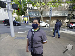 Sonia Guevara poses for a photo, Wednesday, May 18, 2022, outside the Hilton hotel where she works as a housekeeper in downtown Seattle. Many hotels across the United States have done away with daily housekeeping service, making what was already one of the toughest jobs in the hospitality industry even more grueling. (AP Photo/Ted S. Warren)