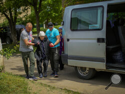 Roman Zhylenkov, left, and another volunteer of Vostok SOS charitable organisation help an elderly woman during an evacuation in Kramatorsk, eastern Ukraine, Thursday, May 26, 2022. Volunteer drivers are risking everything to deliver humanitarian aid to Ukrainians behind the front lines of the war — and to help many of them escape. The routes are dangerous and long and the drivers risk detention, injury or death. (AP Photo/Francisco Seco)