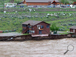 In this image provided by Sam Glotzbach, the flooding Yellowstone River undercuts the river bank, threatening a house and a garage in Gardiner, Mont., on June 13, 2022. (Sam Glotzbach via AP)