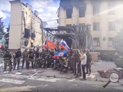 FILE - This photo taken from video provided by Ramzan Kadyrov's Official Telegram channel released on Saturday, July 2, 2022, shows Russian troops including soldiers of Chechen regiment waving Russian and Chechen republic national flags as they pose for a photo in front of a destroyed building in Lysychansk, Ukraine. After more than four months of ferocious fighting, Russia claimed full control over one of the two provinces in Ukraine’s eastern industrial heartland. (Ramzan Kadyrov's Official Telegram chann