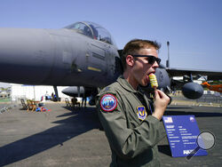 FILE - A member of the military personnel eats an ice cream as he stands past an F15E Strike Eagle fighter jet, on display at the Farnborough Air Show fair in Farnborough, England, Tuesday, July 19, 2022. The future for fighter pilots was on display at the Farnborough International Airshow near London, one of the world’s biggest aviation, defense and aerospace expos. New technologies take on a bigger role in the cockpit, redefining what it means to be a ''Top Gun''. (AP Photo/Alberto Pezzali, File)