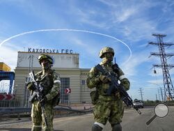 FILE - Russian troops guard an entrance of the Kakhovka Hydroelectric Station, a run-of-the-river power plant on the Dnieper River in Kherson region, southern Ukraine, May 20, 2022. The Kherson region has been under control of the Russian forces since the early days of the Russian military action in Ukraine. Russia and Ukraine have trade blame over shelling of the Zaporizhzhia nuclear power plant, Europe's largest.This photo was taken during a trip organized by the Russian Ministry of Defense. (AP Photo, Fi