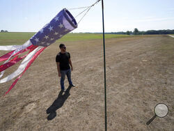 Hay farmer Milan Adams stands in a dry hay field near a wind sock, left, in Exeter, R.I., Tuesday, Aug. 9, 2022. Adams said in prior years it rained in the spring. This year, he said, the dryness started in March, and April was so dry he was nervous about his first cut of hay. (AP Photo/Steven Senne)