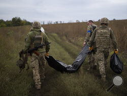 Ukrainian servicemen carry a bag containing the body of a Ukrainian soldier, center, as one of them, right, carries the remains of a body of a Russian soldier in a retaken area near the border with Russia in Kharkiv region, Ukraine, Saturday, Sept. 17, 2022. (AP Photo/Leo Correa)