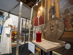 A metal disc shows Pope Emeritus Benedict XVI alongside a painting of him and one of the last cassocks worn by him before his resignation in 2013, according to the director of the Progetto Arte Poli gallery where it is displayed, near the Vatican, Tuesday, Jan. 3, 2023. The Vatican announced that Pope Benedict died on Dec. 31, 2022, aged 95, and that his funeral will be held on Thursday, Jan. 5, 2023. (AP Photo/Ben Curtis)