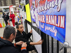 Kayla Adeniji, center, wife of Cincinnati Bengals offensive lineman Hakeem Adeniji, tapes up a sign she made in support of Buffalo Bills safety Damar Hamlin outside UC Medical Center, Thursday, Jan. 5, 2023, in Cincinnati. Hamlin, who remains hospitalized at the center, has shown what physicians treating him are calling "remarkable improvement over the last 24 hours," the team announced on Thursday, three days after the player went into cardiac arrest and had to be resuscitated on the field. (AP Photo/Joshu