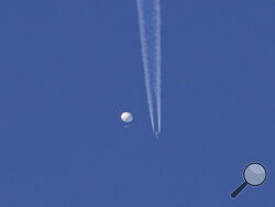 In this photo provided by Brian Branch, a large balloon drifts above the Kingstown, N.C. area, with an airplane and its contrail seen below it. The United States says it is a Chinese spy balloon moving east over America at an altitude of about 60,000 feet (18,600 meters), but China insists the balloon is just an errant civilian airshipused mainly for meteorological research that went off course due to winds and has only limited “self-steering” capabilities. (Brian Branch via AP)