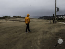 A man walks through a windstorm at Ocean Beach on a stormy morning in San Francisco on Tuesday, March 14, 2023. (Gabrielle Lurie/San Francisco Chronicle via AP)