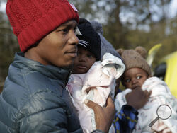 Haitian migrant Gerson Solay, 28, carries his daughter, Bianca, as he and his family cross into Canada at the non-official Roxham Road border crossing north of Champlain, N.Y., on Friday, March 24, 2023. A new US-Canadian migration agreement closes a loophole that has allowed migrants who enter Canada away from official border posts to stay in the country while awaiting an asylum decision. (AP Photo/Hasan Jamali)