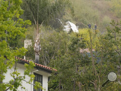 National Transportation Safety Board investigators inspect a downed plane on a steep hill above a home on Beverly Glen Circle in Los Angeles, Sunday, April 30, 2023. Fire department officials said a person was found dead following an intensive search for the single-engine airplane that crashed in a foggy area Saturday night. (AP Photo/Damian Dovarganes)