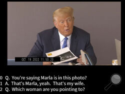 In this image taken from video released by Kaplan Hecker & Fink, former President Donald holds a photograph, presented as evidence during his Oct. 19, 2022 deposition, that shows E. Jean Carroll and her then-husband John Johnson meeting Trump and his wife Ivanka at an event in the 1980s. In his deposition, Trump mistook Carroll as Marla Maples, his now ex-wife, when shown the image. The video recording of Trump being questioned about the rape allegations against him was made public for the first time Friday